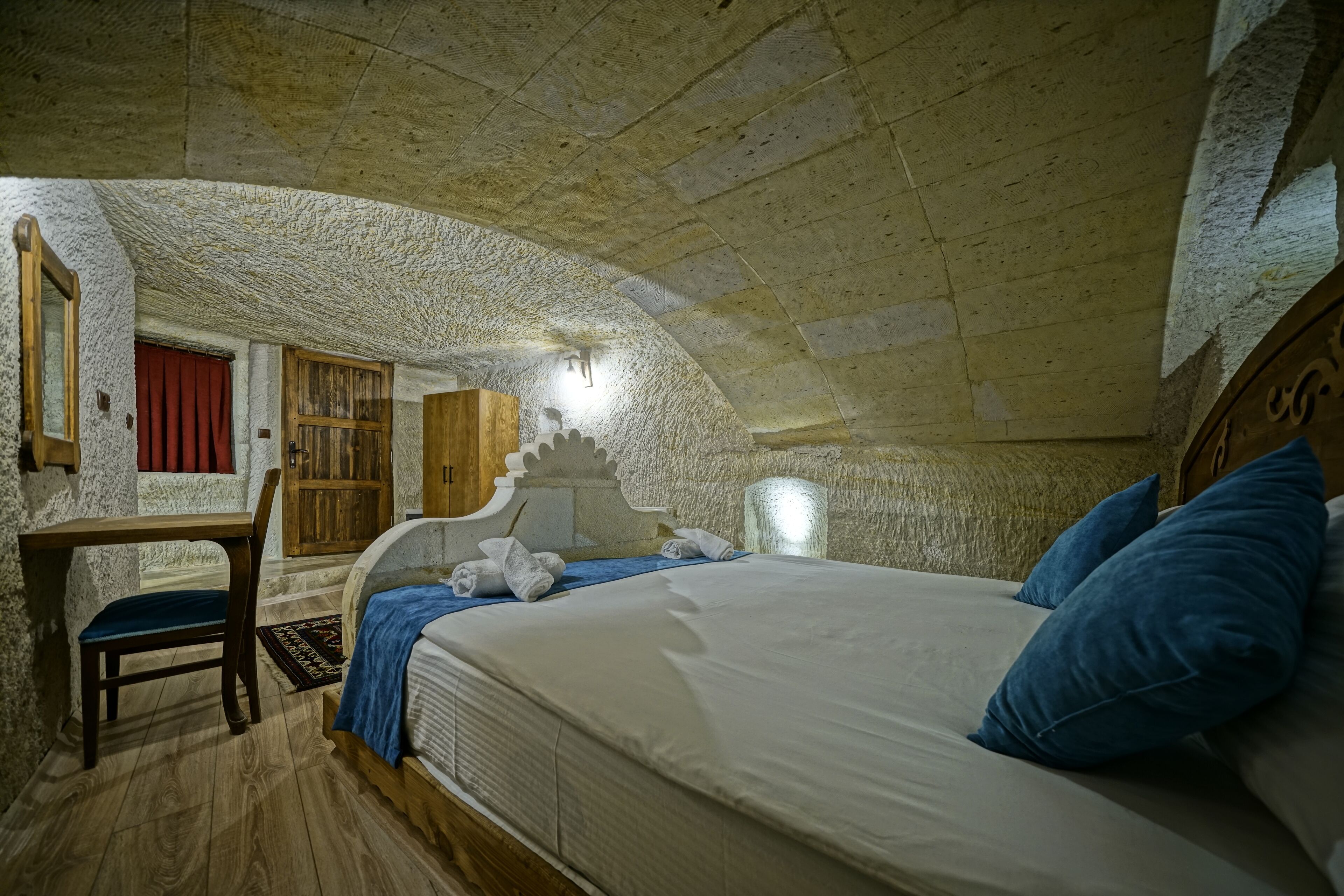 A bedroom with a stone ceiling, a wooden bed, a desk, and a chair.