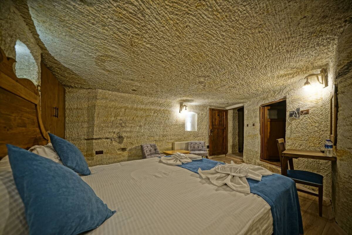 A stone-walled bedroom with a bed, pillows, a table, and a chair.