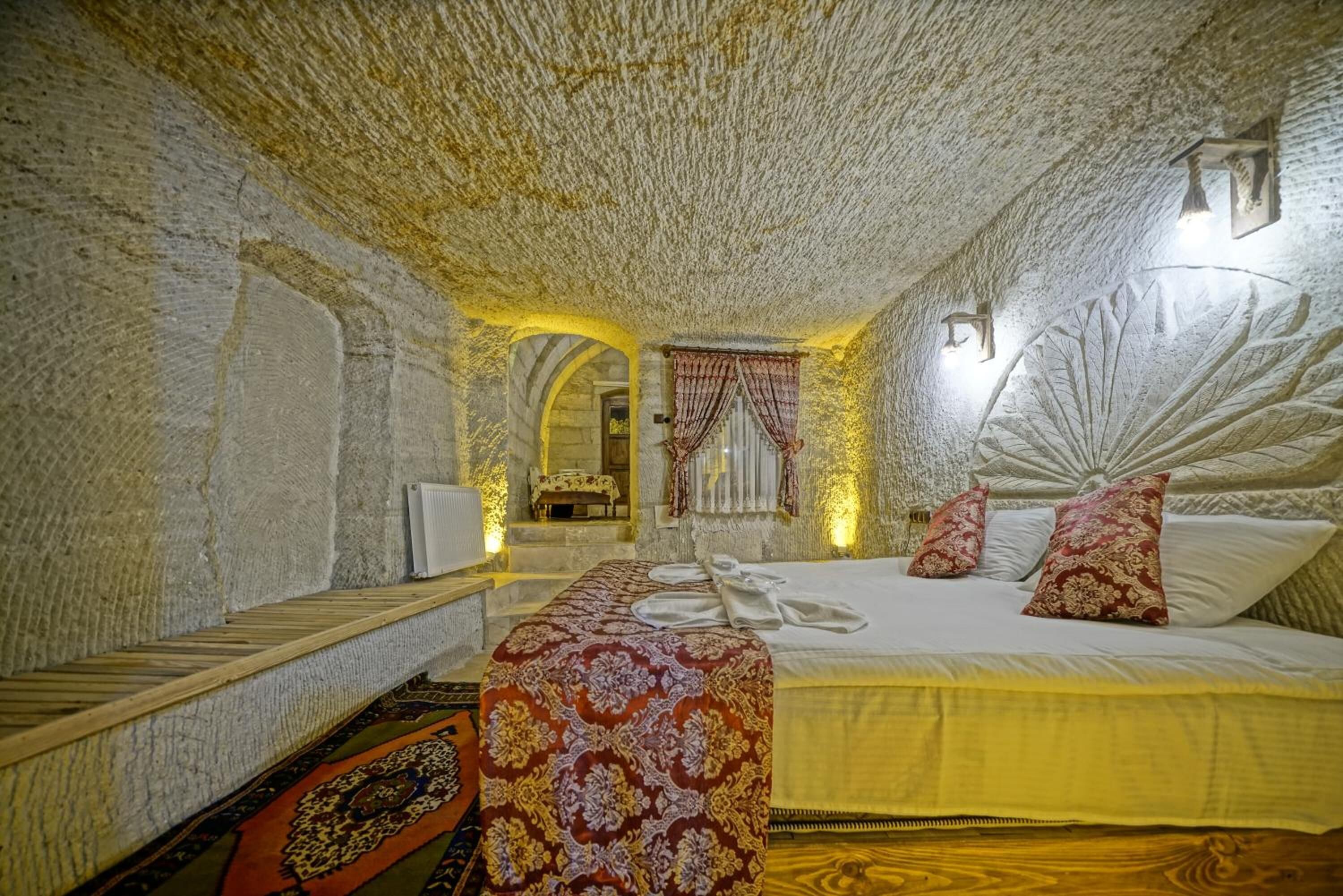 A room with a stone ceiling, a bed with patterned bedding, a bench, and a small table.