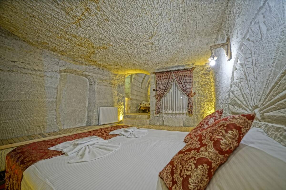A room with a large bed, a stone wall, and a window with curtains.