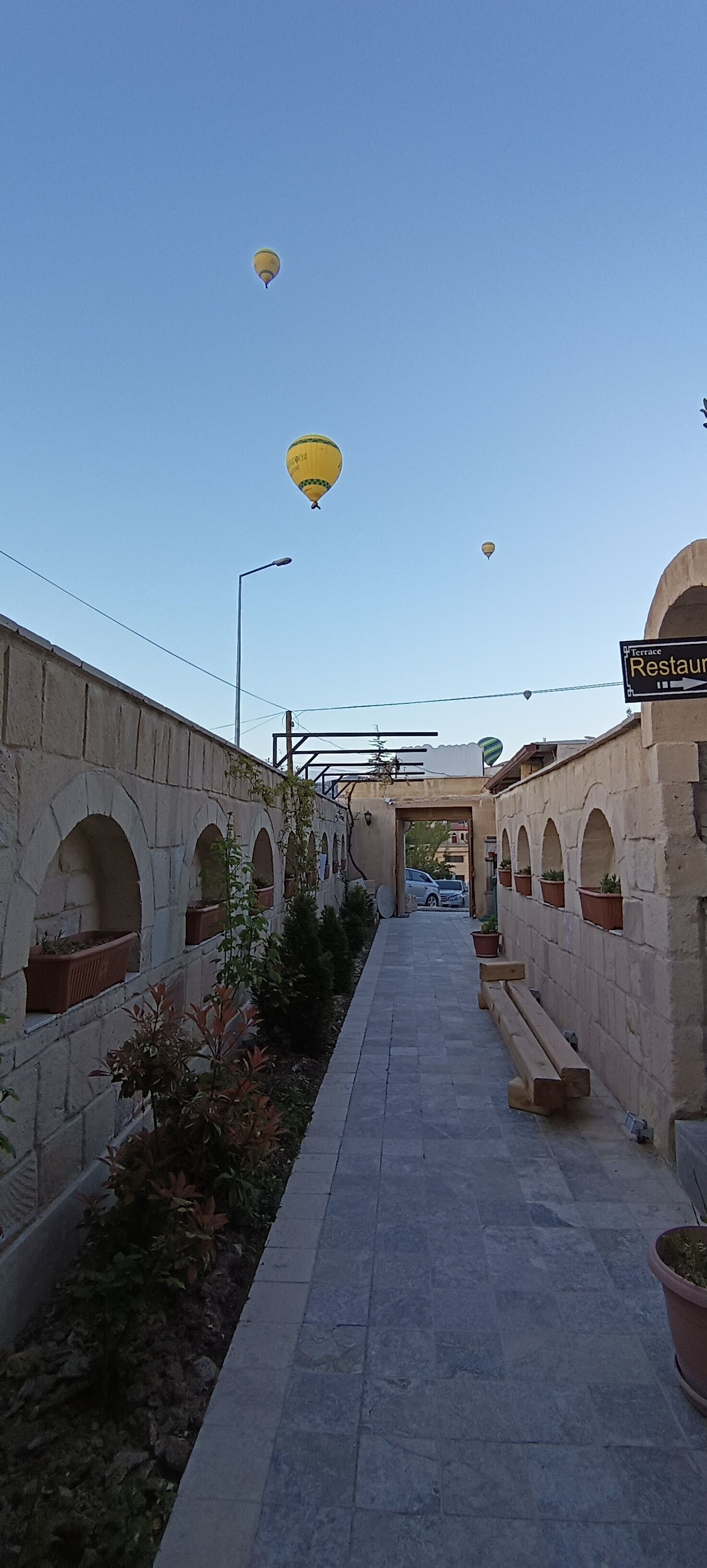 A stone pathway with arches, potted plants, and a sign for a terrace restaurant.