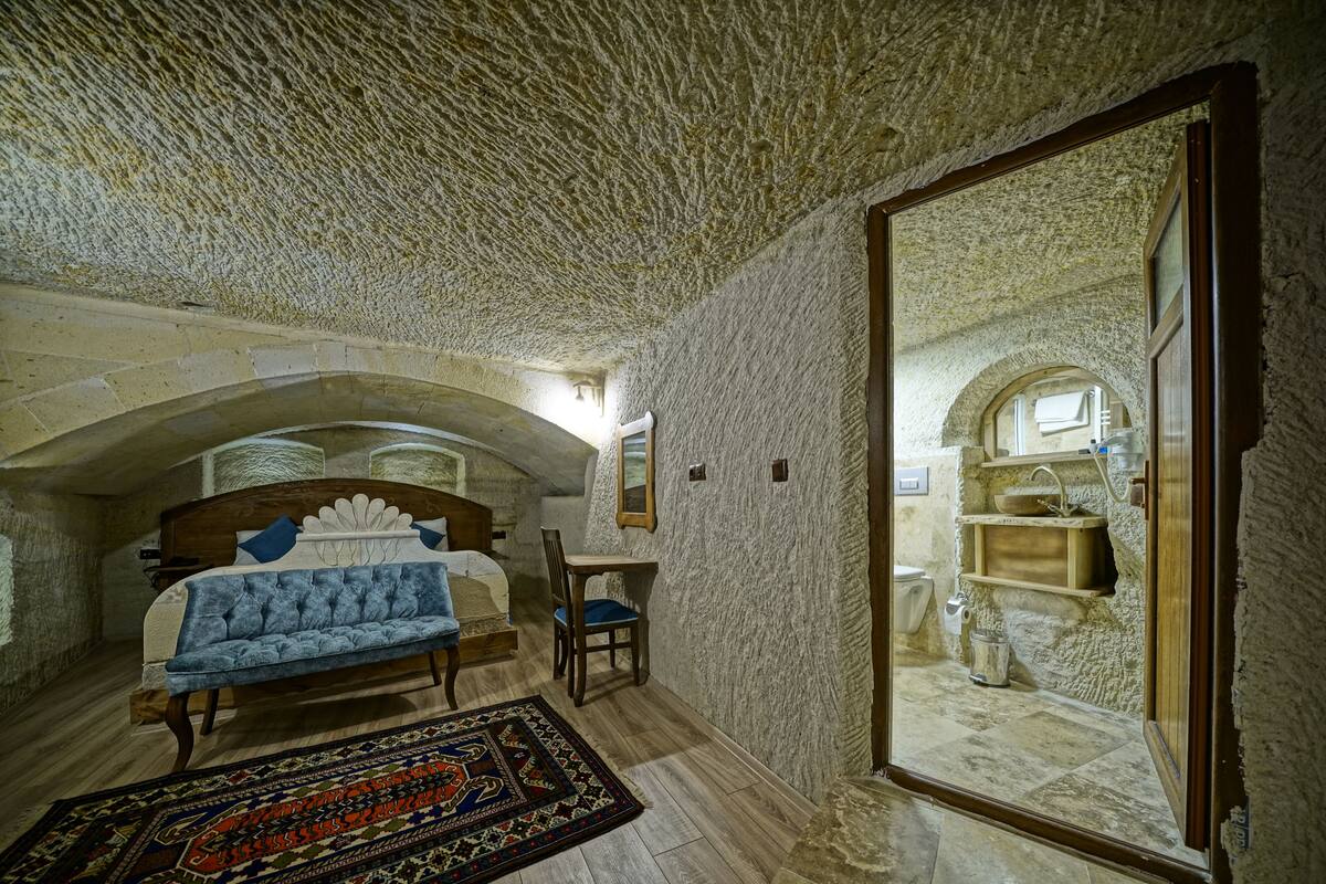 A bedroom with a stone ceiling, a wooden bed, a blue upholstered sofa, a chair, and a patterned rug.