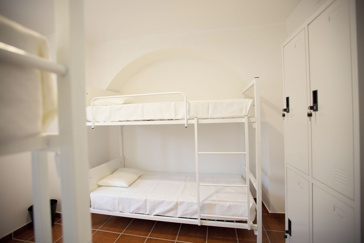Habitación con literas, cabecero blanco, mesita de noche pequeña y armario con múltiples puertas.