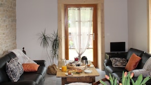 A rustic living room with exposed wooden beams, a stone wall, and a dining area with a table set for two. - Chambres D'Hôtes Bered Vuillemin (Baume-les-Dames)