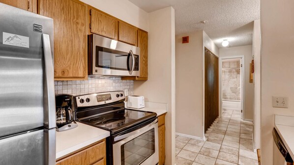 Efficient kitchen with stainless steel appliances, a stove, microwave, and toaster, set against a backdrop of wooden cabinetry and a tiled floor.