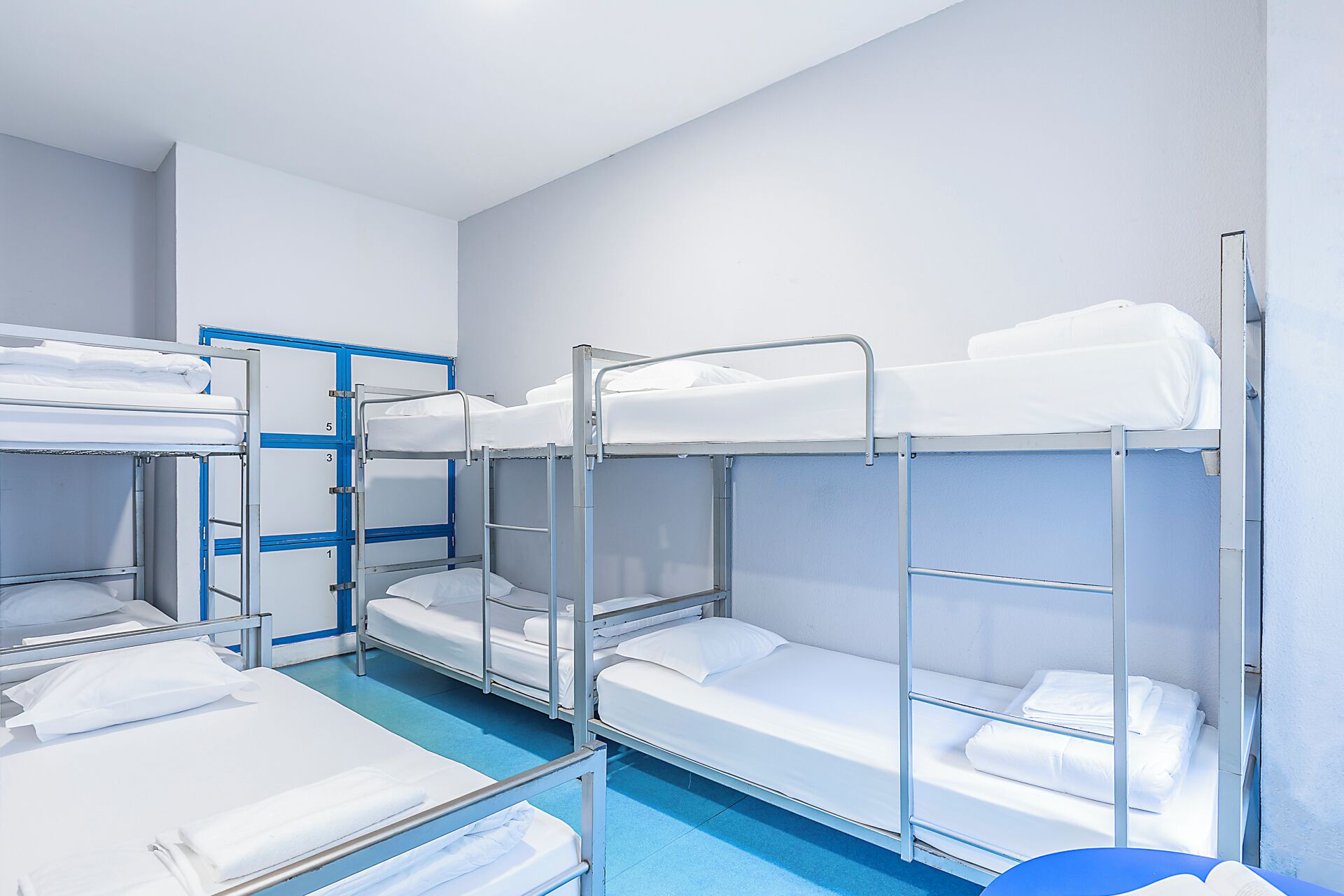 A bunk room with metal bunk beds, white bedding, and a blue floor.