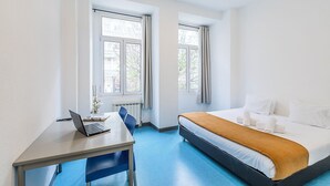 A hotel room with a bed, a desk with a laptop, two windows, and a radiator. - HI Lisboa – Pousada de Juventude - Hostel (Lisbon)