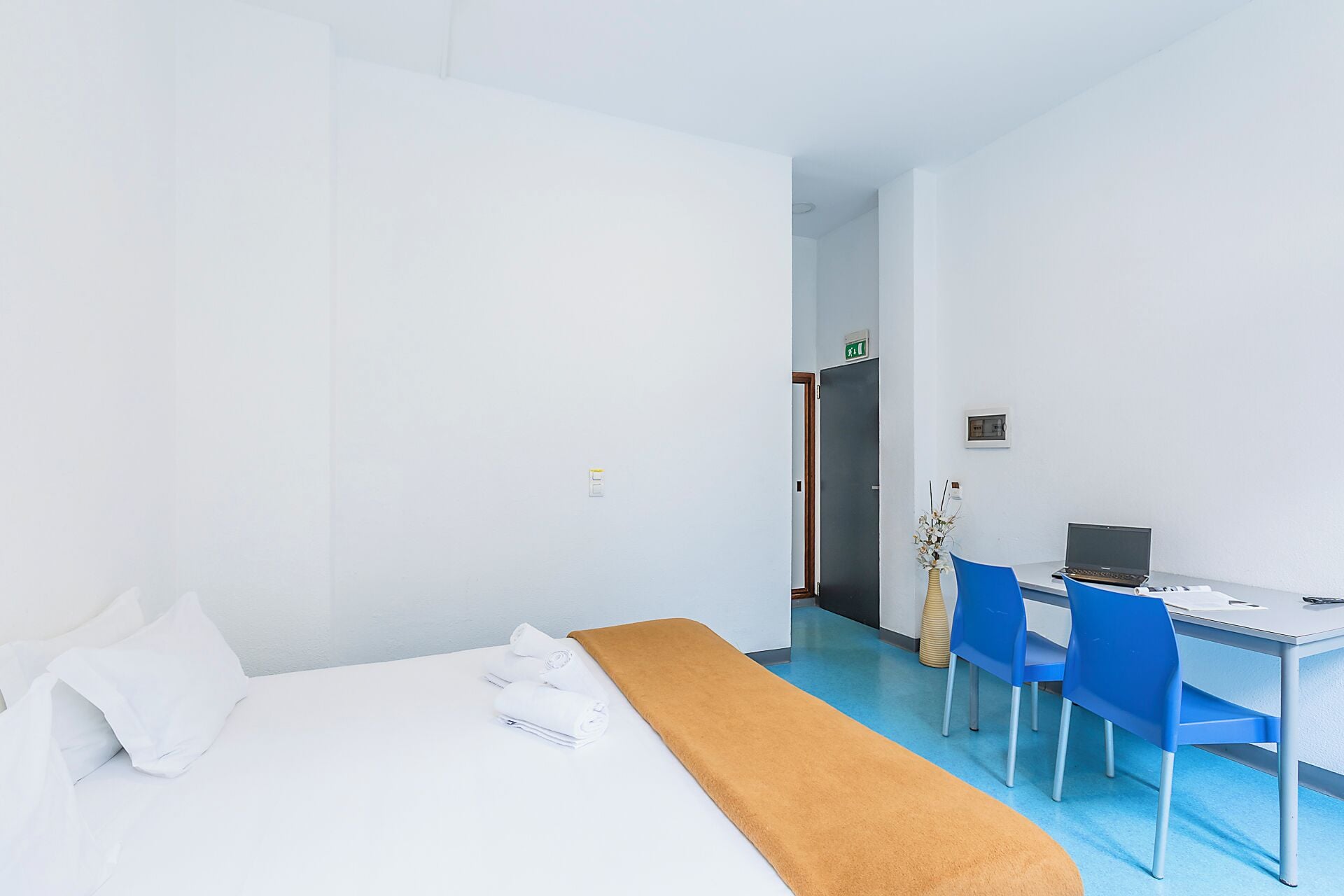 Habitación de hotel con cama, escritorio y laptop, además de una silla.