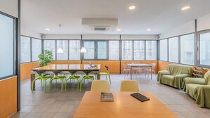 A modern meeting room with a wooden table, green chairs, a sofa, and large windows. - HI Lisboa – Pousada de Juventude - Hostel (Lisbon)
