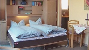 A compact bedroom with a bed, built-in wooden shelves, a small desk, and a chair. - Apartmenthaus Padua (Büsum)