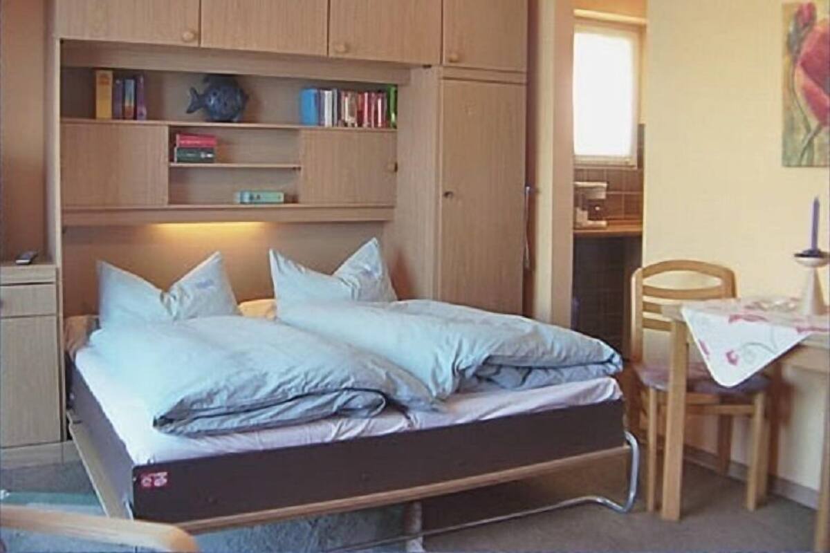 A compact bedroom with a bed, built-in wooden shelves, a small desk, and a chair.