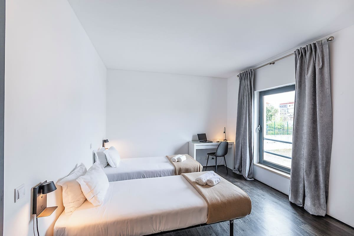 Ein Hotelzimmer mit zwei Betten, einem Schreibtisch, einem Stuhl und einem Fenster mit Vorhängen.