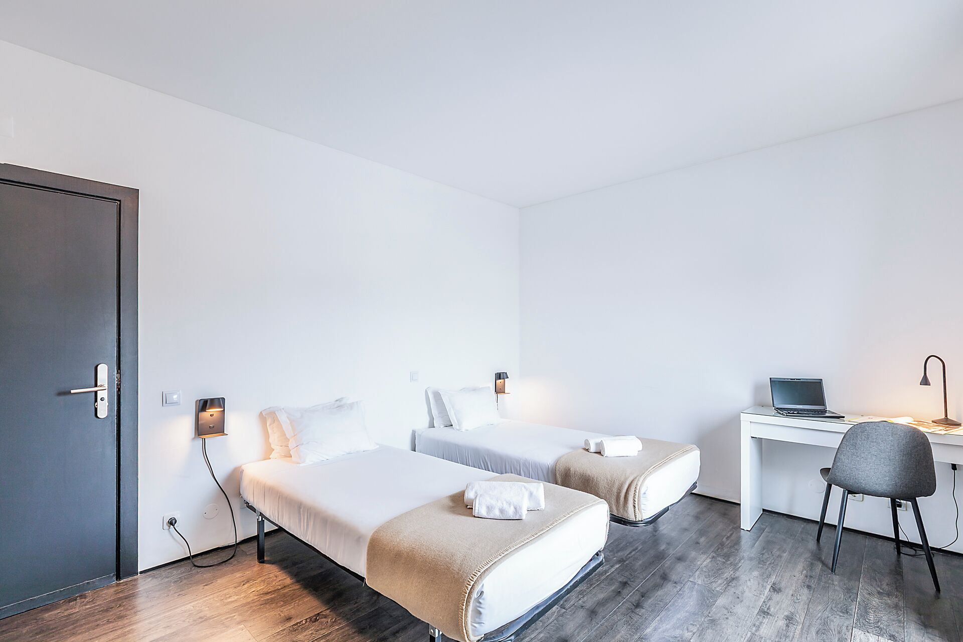 A hotel room with two beds, a desk, a chair, and a laptop.