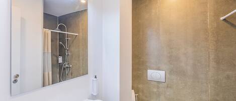 A modern bathroom with a white sink, a mirror, a shower, and a toilet.