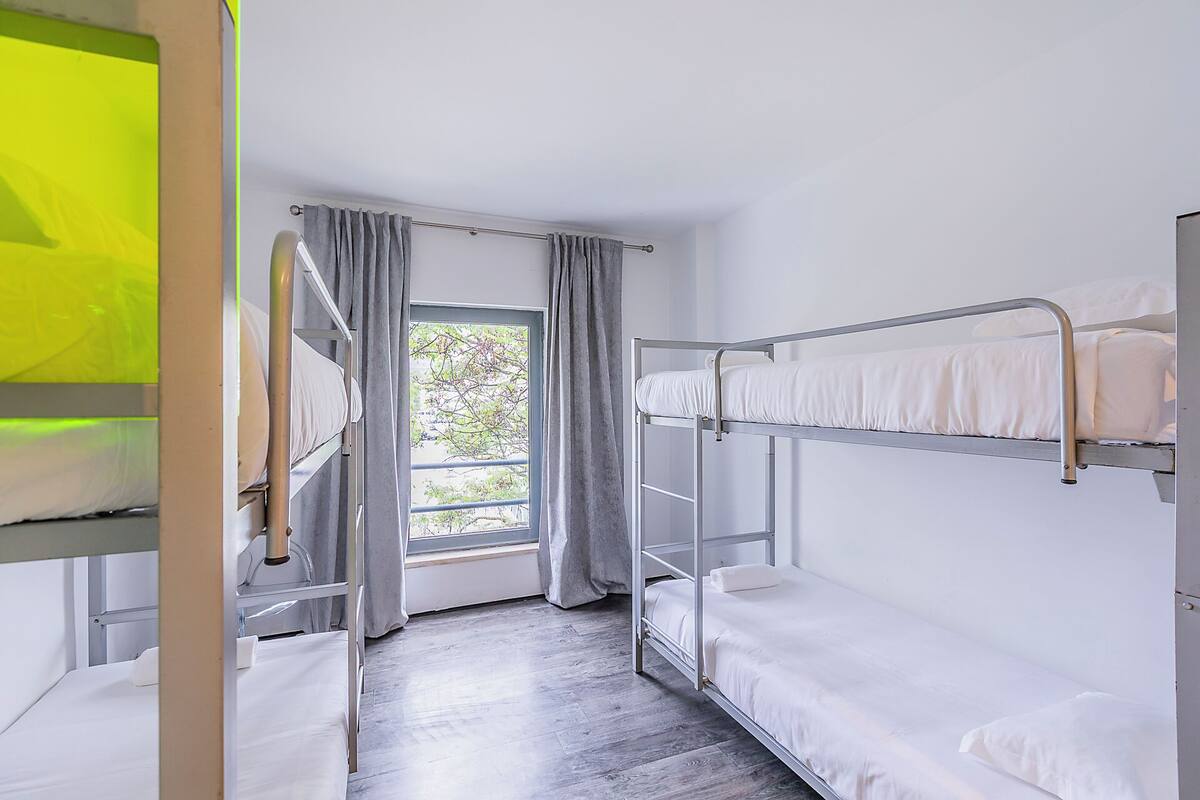Ein Schlafsaalzimmer mit Etagenbetten, einem Fenster mit Vorhängen und einem Holzboden.