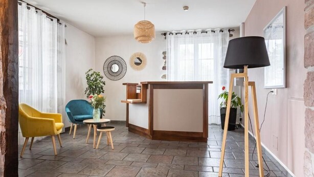 Een zithoek met een gele fauteuil, een blauwe fauteuil, een bijzettafeltje met een vaas, een houten dressoir en een vloerlamp.