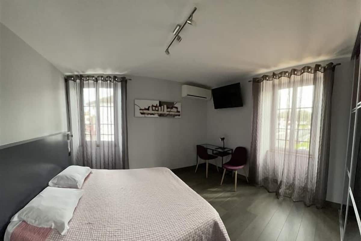 Une chambre d’hôtel comprenant un lit, un bureau avec une chaise, un téléviseur à écran plat et des rideaux.