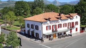 Een wit gebouw met rode luiken en een bord waarop staat 'HOTEL RESTAURANT MENDY'.