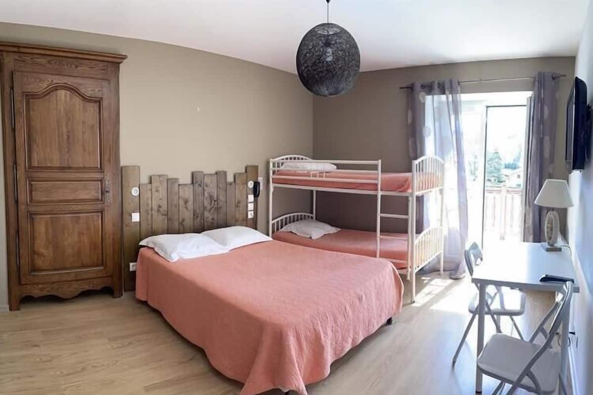 Une chambre avec deux lits superposés, une armoire en bois, un bureau avec une chaise et un luminaire suspendu.
