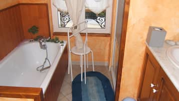 A bathroom with a bathtub, a white sink, a wooden cabinet, a blue rug, and a window with a curtain.