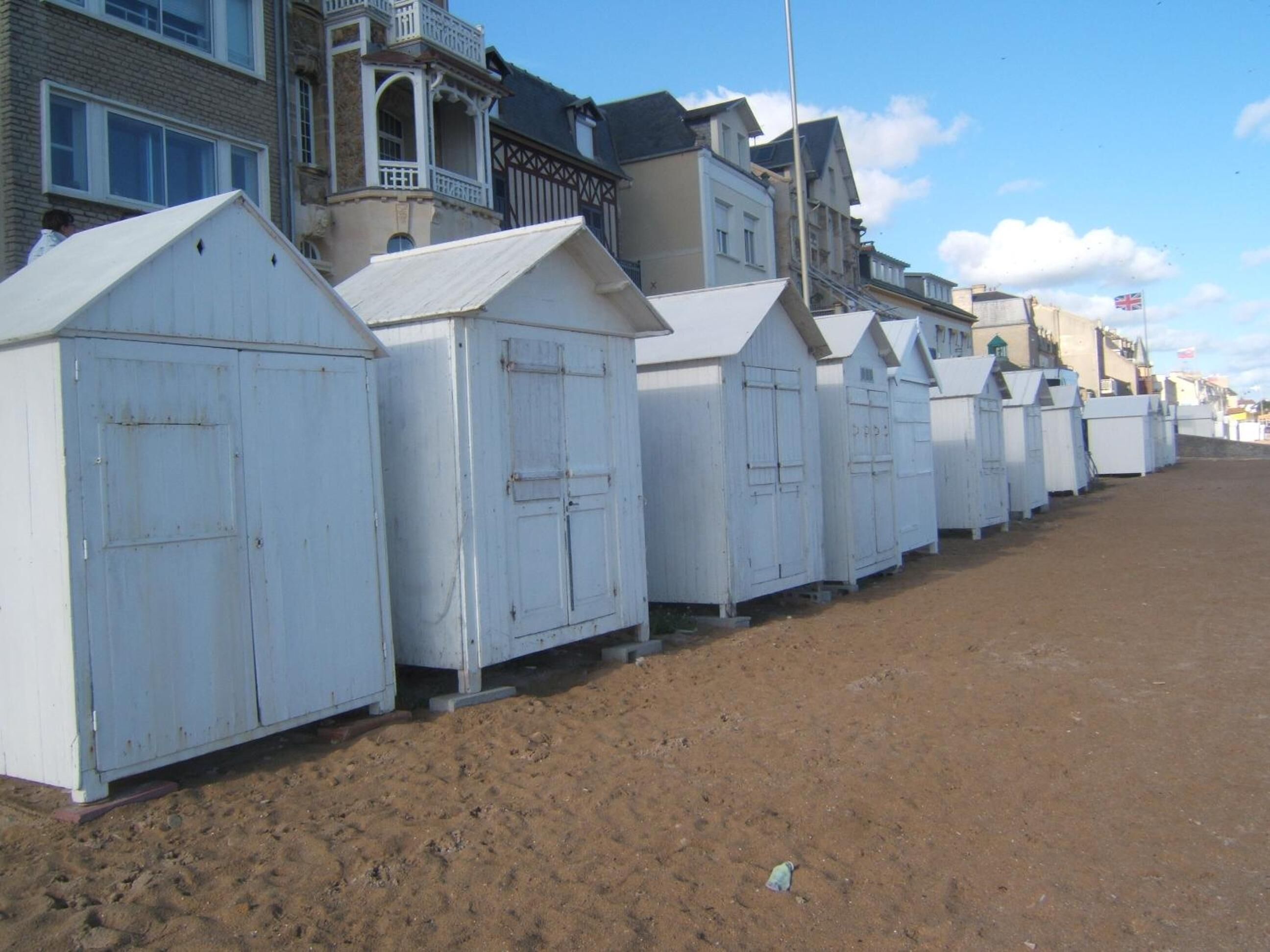 Een rij witte strandhutten met zand ertussen, voor een achtergrond van woongebouwen.