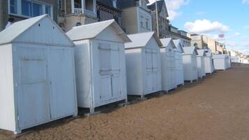 Een rij witte strandhutten met zand ertussen, voor een achtergrond van woongebouwen.