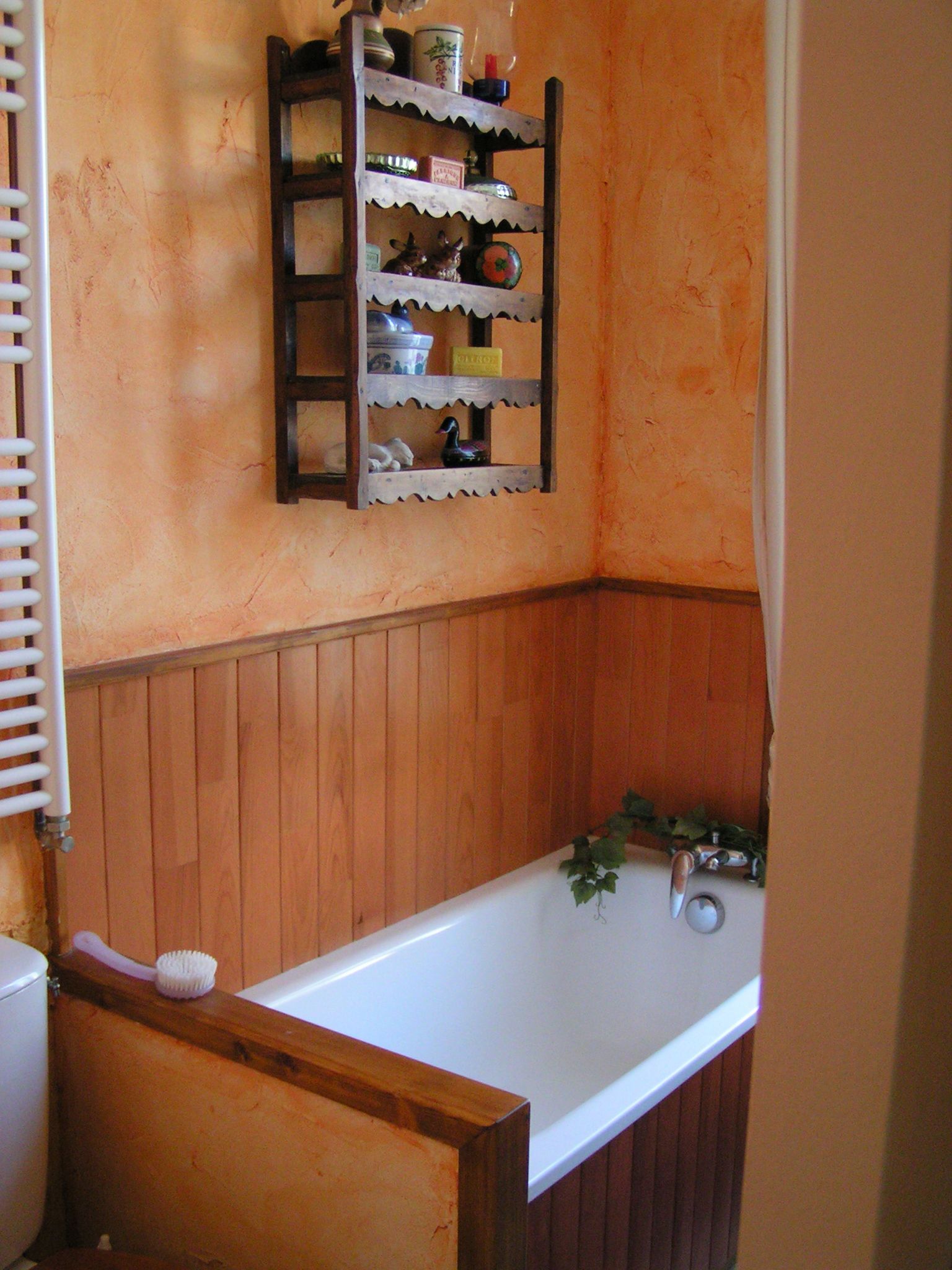 Een badkamer met een houten wastafelmeubel, een witte badkuip en een plank met diverse spullen.