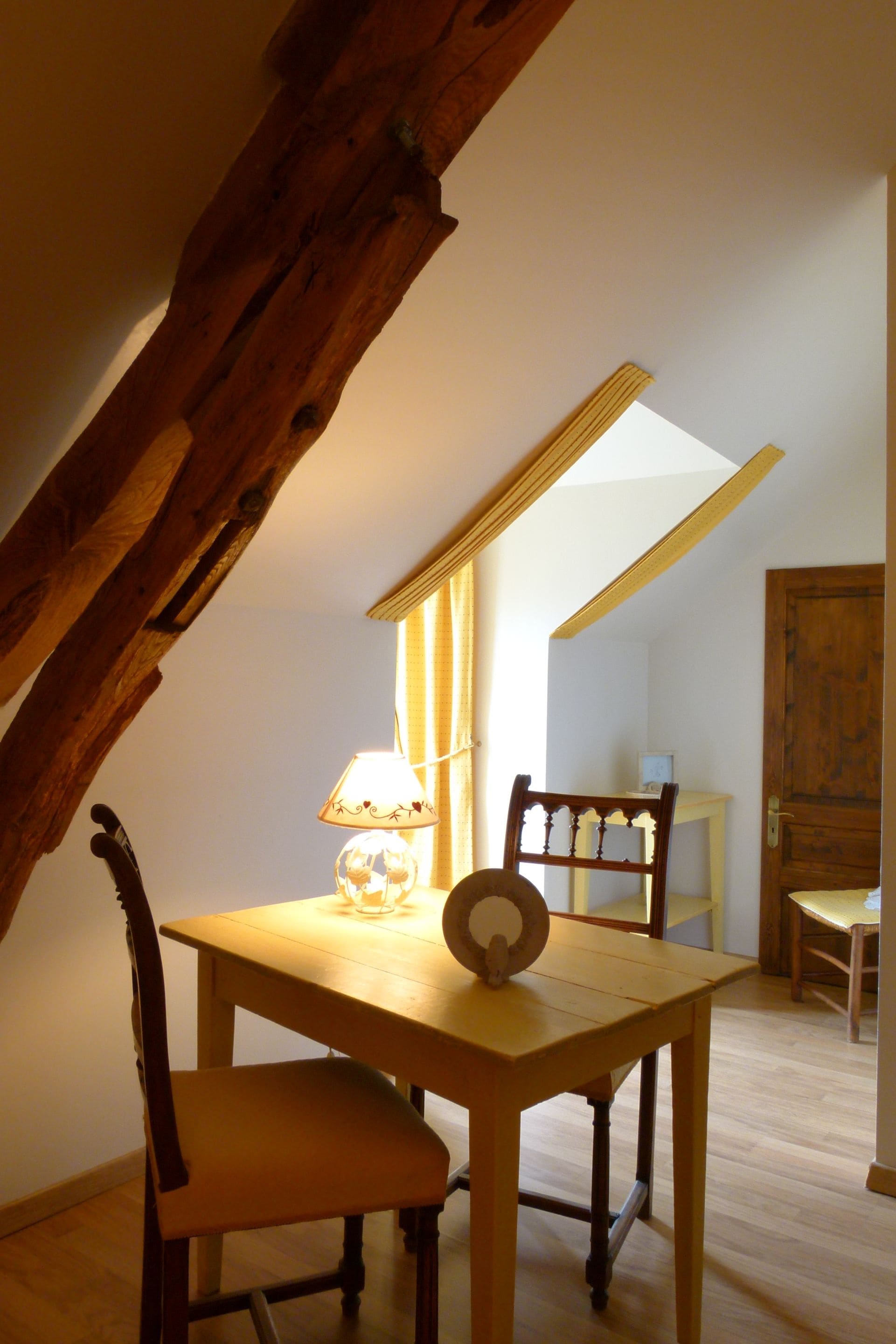 Una mesa de comedor de madera con una lámpara y sillas en una habitación con techos inclinados y vigas de madera.