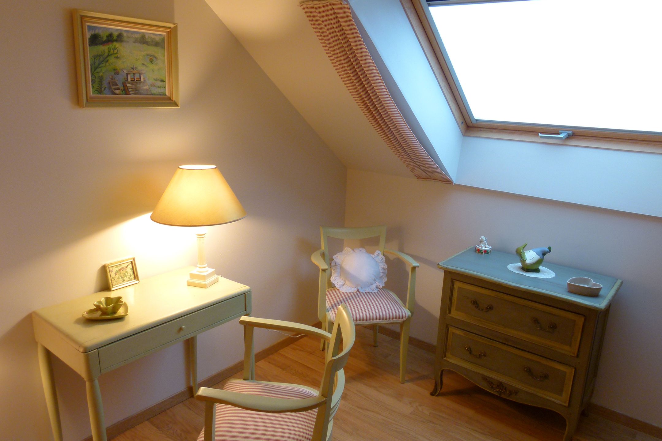 A cozy room with a desk, chair, bedside table, and a window with blinds.