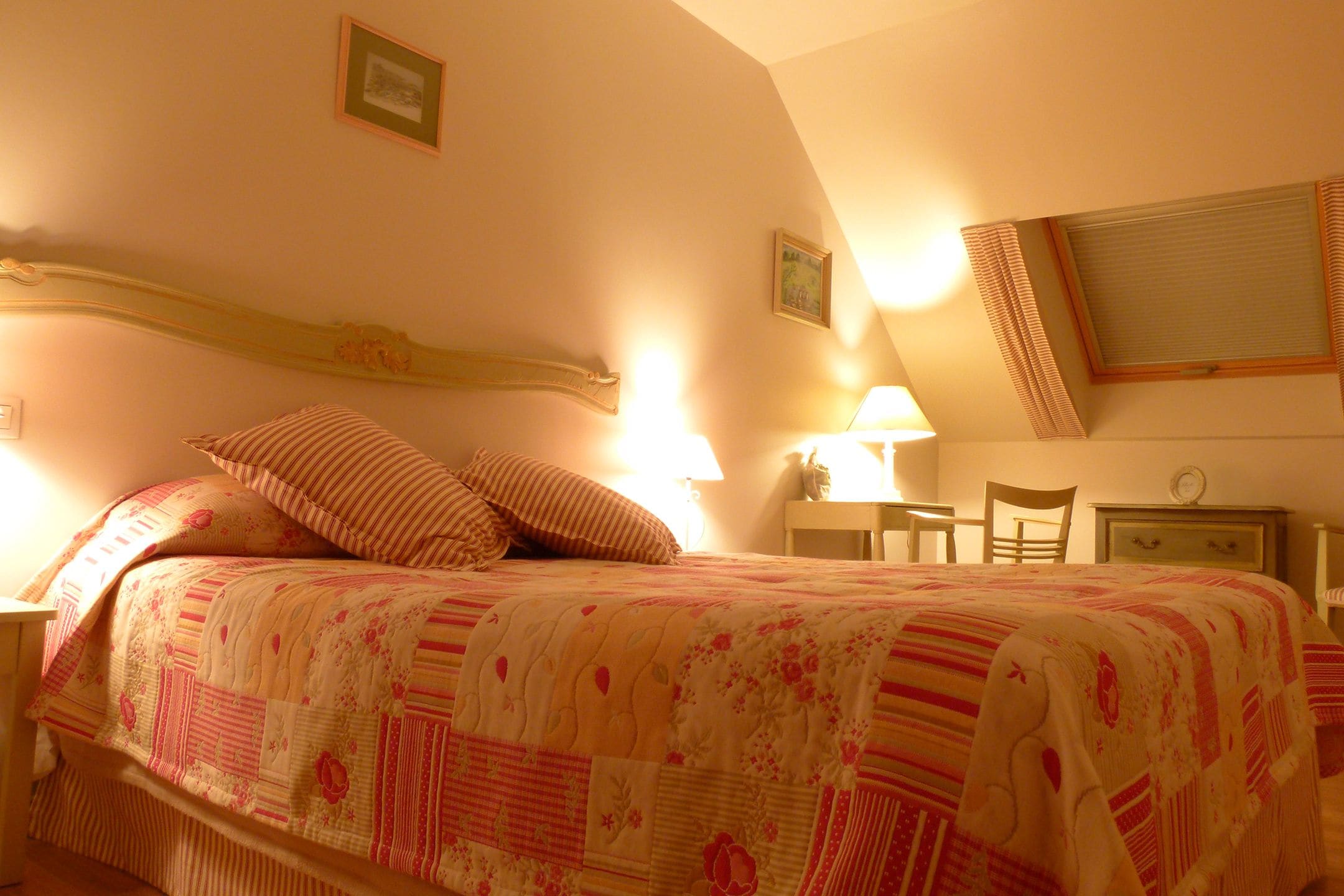 A bedroom with a bed, pillows, a nightstand, a lamp, a chair, and a desk.