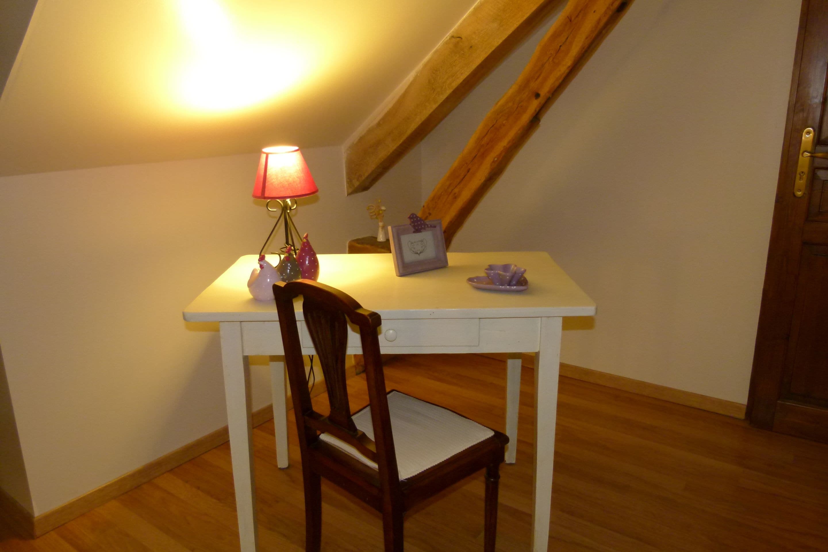 A small, white desk with a chair, a lamp, and a few decorative items.