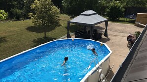 An above-ground swimming pool with two people swimming, surrounded by a grassy yard and trees. - La Ferme de Marpalu (La Ferte-Saint-Cyr)