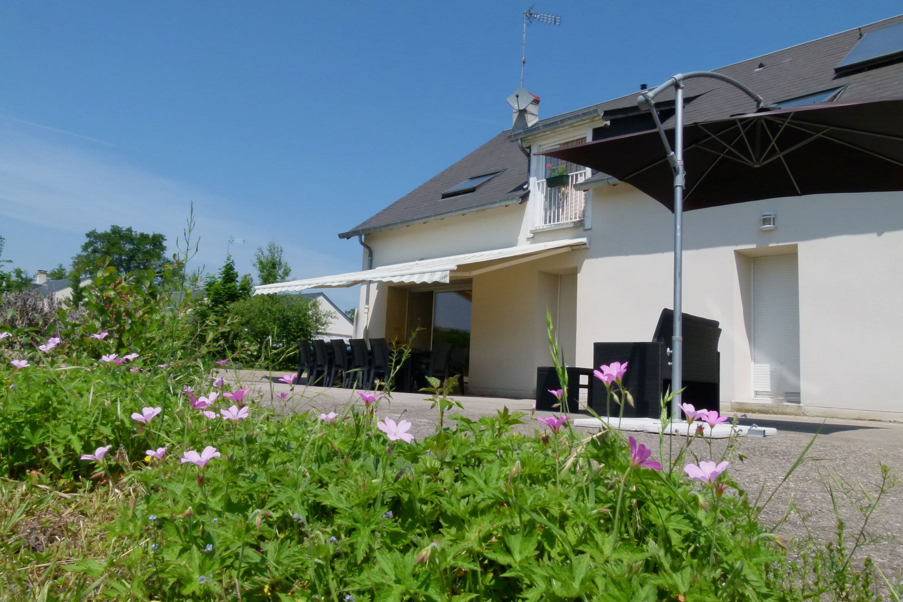 Una casa con porche cubierto, mobiliario de exterior y jardín con flores.