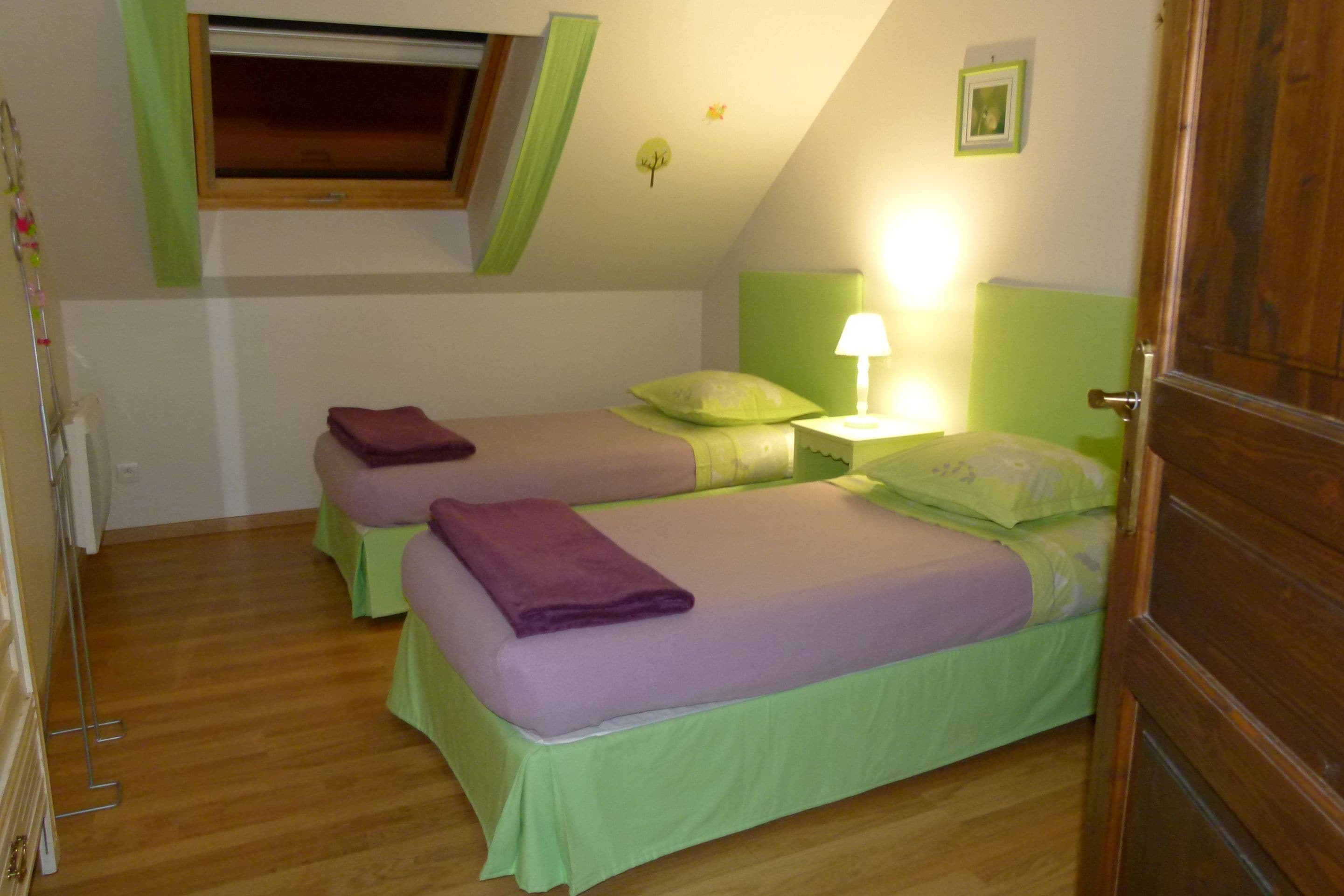 Una habitación con dos camas, una ventana, una puerta y una mesita con lámpara.