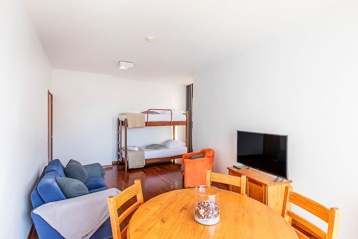 Una habitación con literas, un sofá, un televisor y una mesa de comedor.