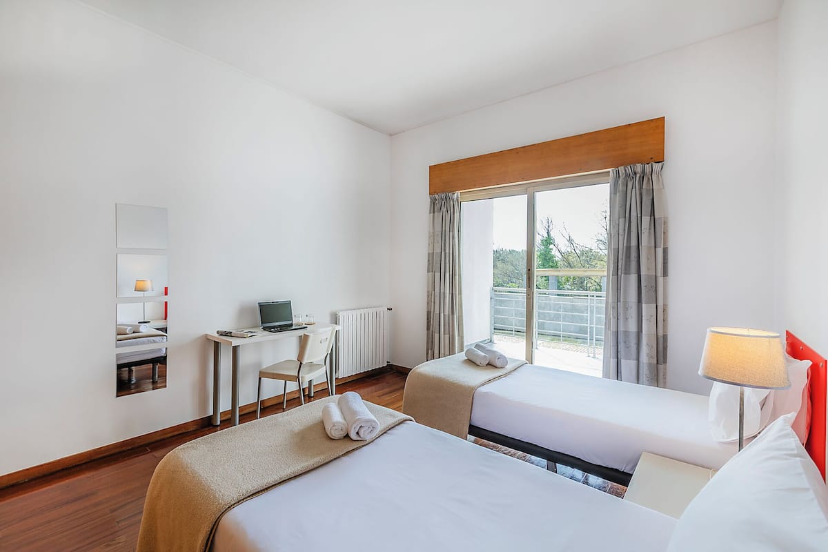 Une chambre d’hôtel avec un lit, un bureau avec un ordinateur portable, une chaise et une fenêtre avec des rideaux.