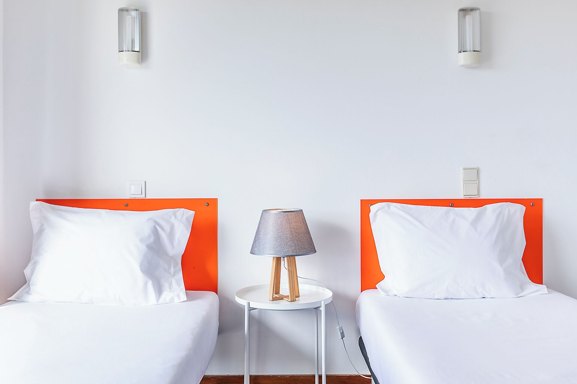 A hotel room with two beds, a small table with a lamp, and two wall-mounted light fixtures.