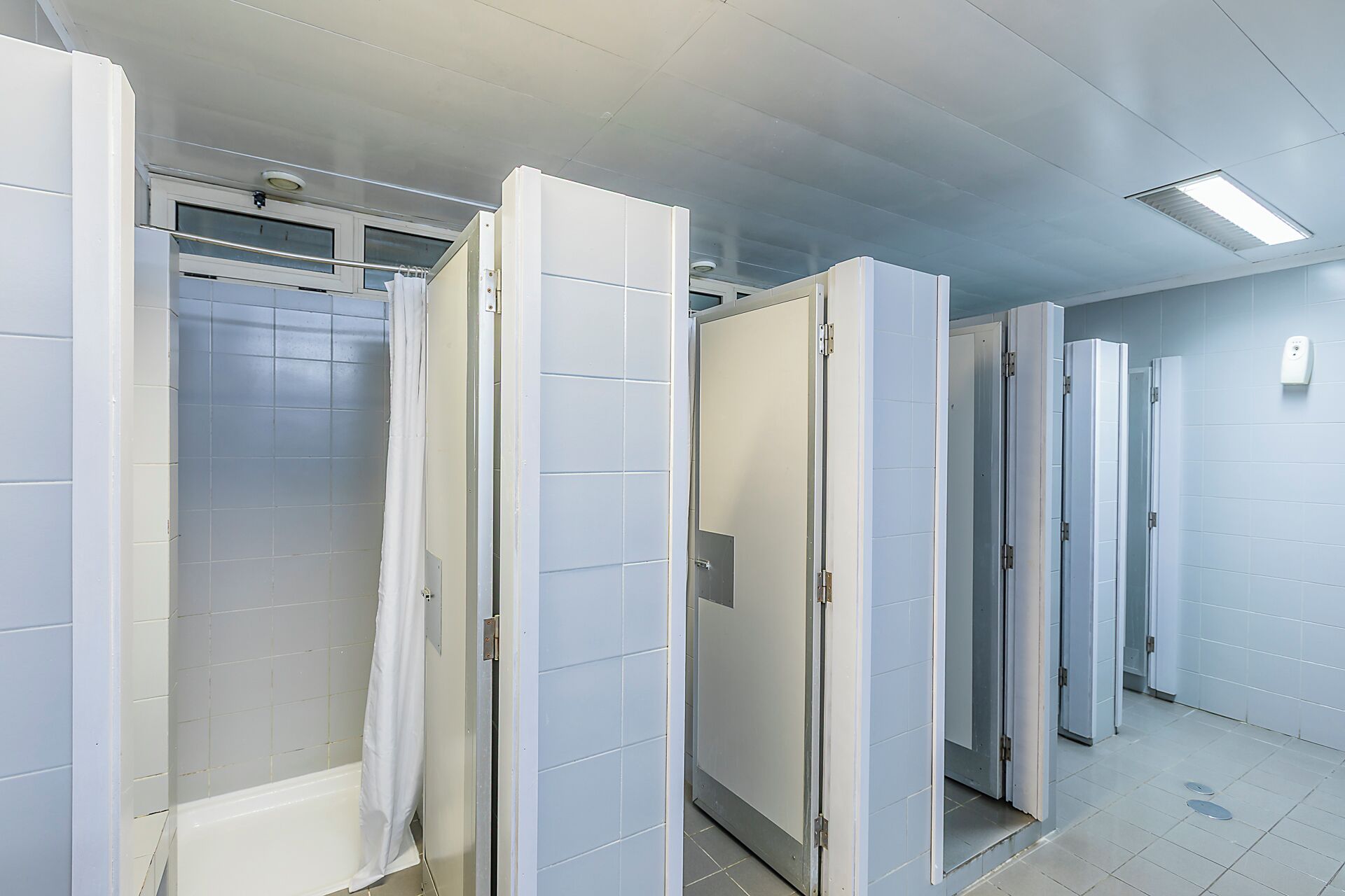 Un couloir avec plusieurs portes, un espace douche et un sol carrelé.