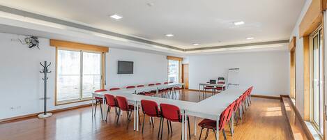 Un salón de conferencias con una larga mesa, sillas rojas, una pizarra y un televisor en la pared.