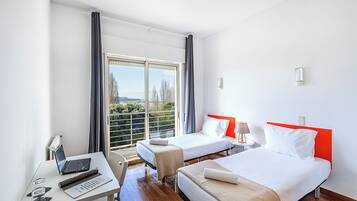 Ett hotellrum med två sängar, ett skrivbord med en bärbar dator, en stol och utsikt över grönområden utanför.