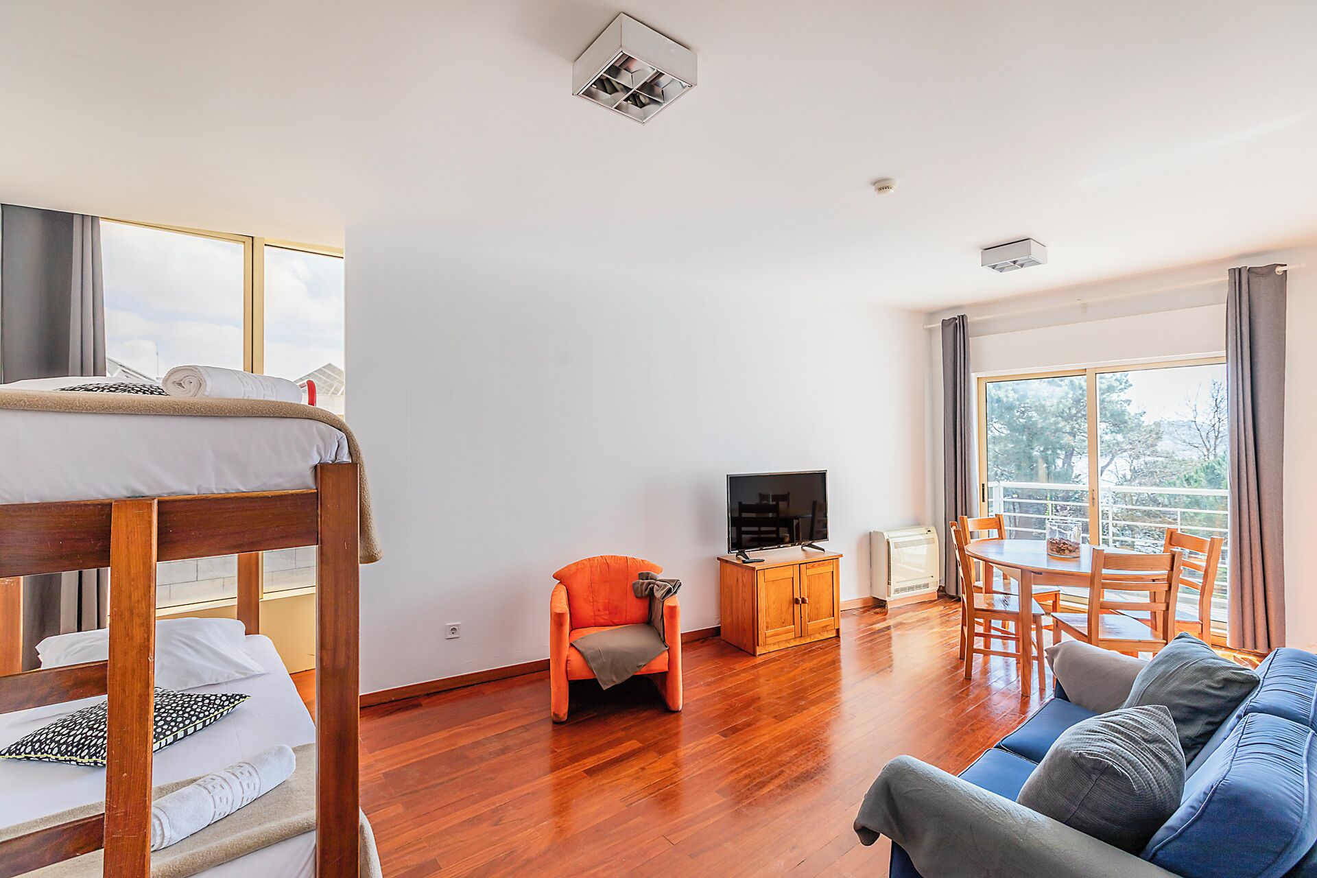A room with a bunk bed, a TV, a sofa, a dining table, and a view of the outdoors.