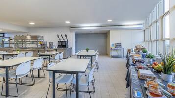 A cafeteria with tables and chairs, a kitchen area, and a buffet table with food items.