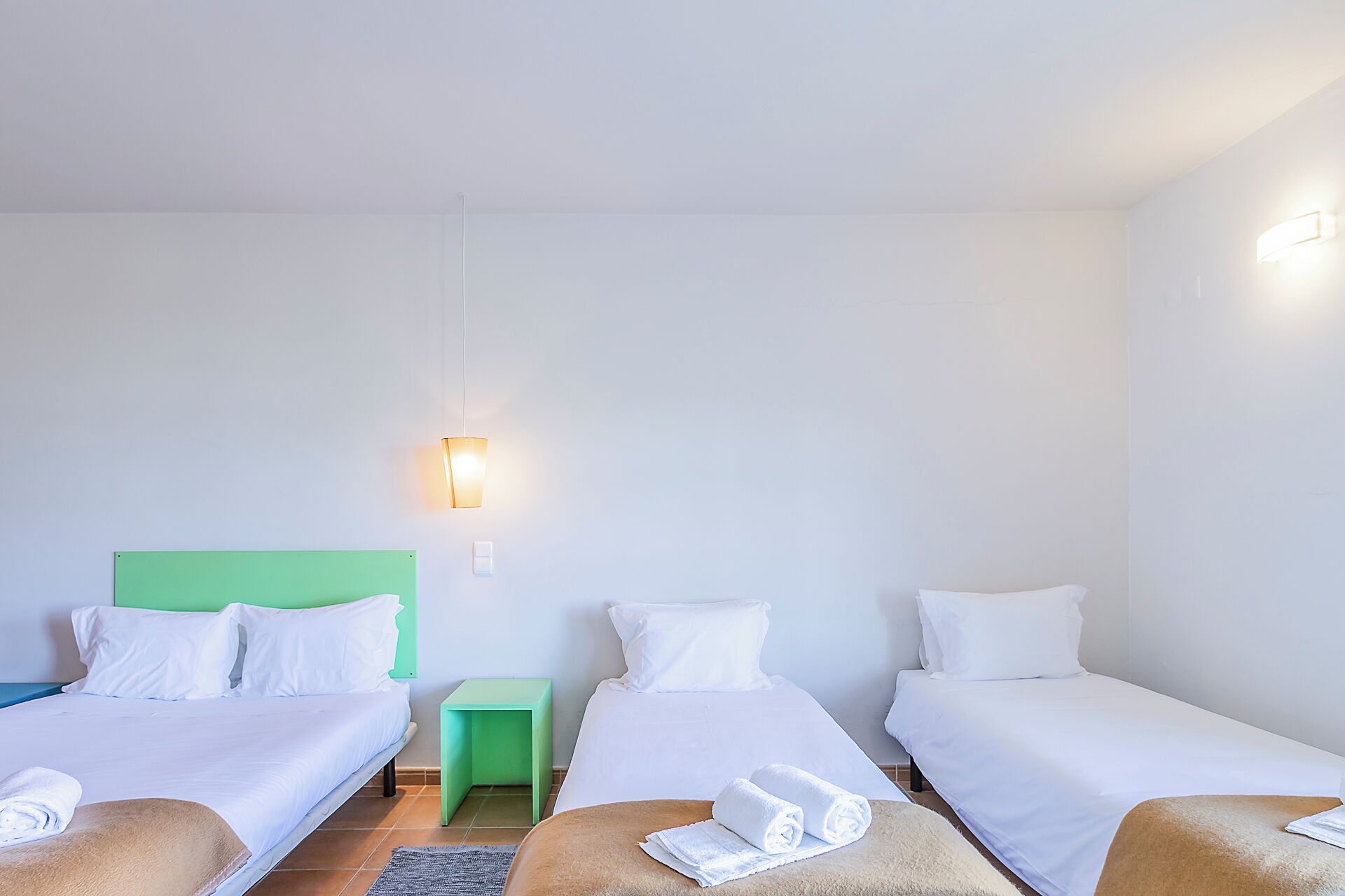 Una camera d'albergo con tre letti singoli, un comodino verde e un lampadario a parete.