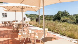 Une terrasse extérieure avec des tables et des chaises, protégée par de grands parasols, et offrant une vue sur un paysage vallonné.