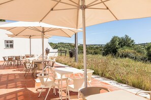 Una terrazza esterna con tavoli e sedie sotto grandi ombrelloni, con vista su un paesaggio collinare.