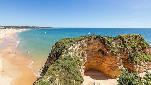 Un paysage côtier caractérisé par une plage de sable, une mer d’un bleu limpide et une falaise imposante.