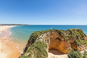 Paisaje costero con una playa arenosa, mar azul cristalino y una imponente formación rocosa.