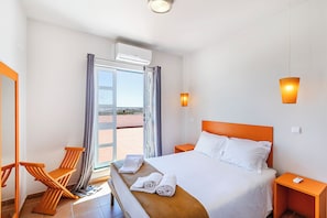 Camera d'albergo con un letto, una sedia, un comodino, un condizionatore d'aria e vista panoramica attraverso una porta vetrata.