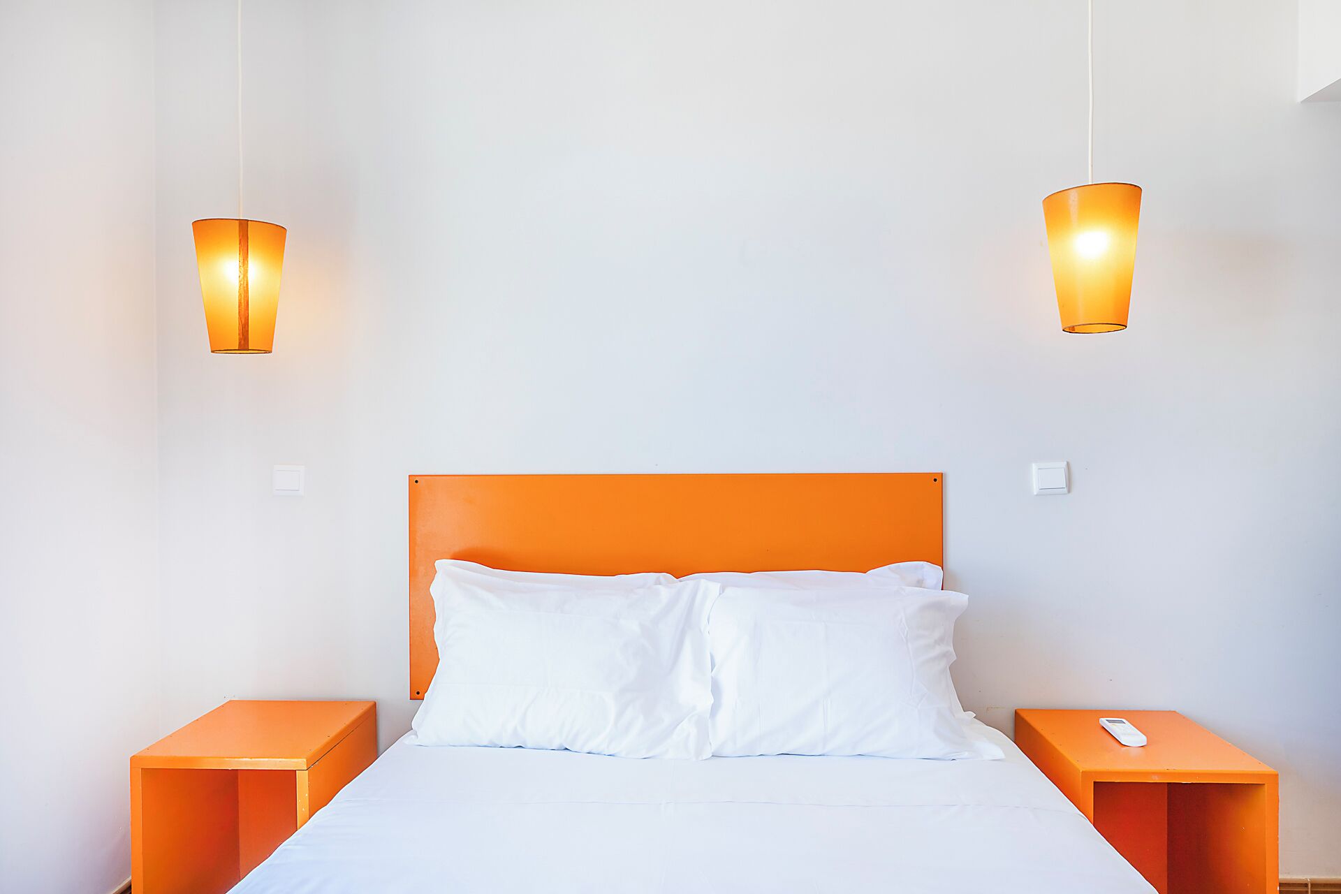 Un lit avec une tête de lit orange, deux tables de chevet et deux lampes fixées au mur.