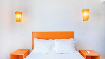 Un lit avec une tête de lit orange, deux tables de chevet et deux lampes fixées au mur.